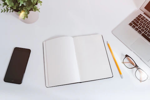 Carnet ouvert, ordinateur portable et téléphone sur un bureau blanc